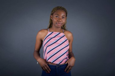 Çekici, başarılı, Afro-Amerikalı bir kadının portresi. Kendinden emin bir ifadeyle gülümsüyor, el ele tutuşuyor ve gri duvarın önünde duruyor..