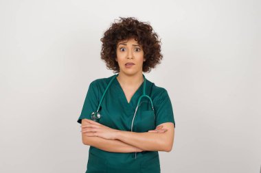 Tıbbi üniforma giyen, dudağını ısıran ve endişeli görünen güzel bir Arap doktor portresi. 