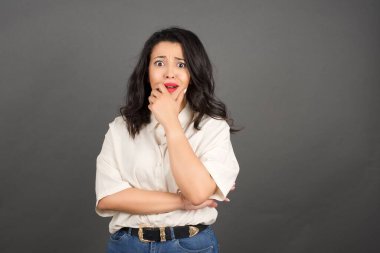 Güzel esmer kadın korkuyor. Gri arkaplanda duruyor.