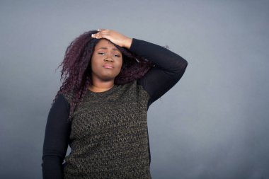 Tüh, ne yaptım ben? Güzel afro-amerikan kadın gündelik giysiler içinde korkmuş ve pişmanlık dolu bir ifadeyle el ele tutuşuyor. Gri arka planda dikilen günlük giysiler giyiyor..