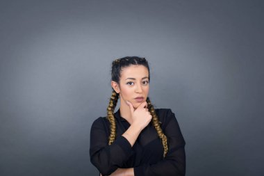 Düşünceli gülümseyen bir kadının portresi elini çenesinin altında tutar, doğrudan kameraya bakar, ilgiyle karışık bir şey dinler, sıradan giyinir, gri duvara karşı poz verir..