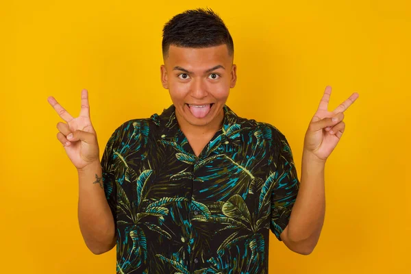 Gri arka planda, iyimser bir gülümsemeyle izole edilmiş, iki eliyle barış ya da zafer jesti yapan, dost canlısı görünen genç İspanyol erkek portresi. V işareti.