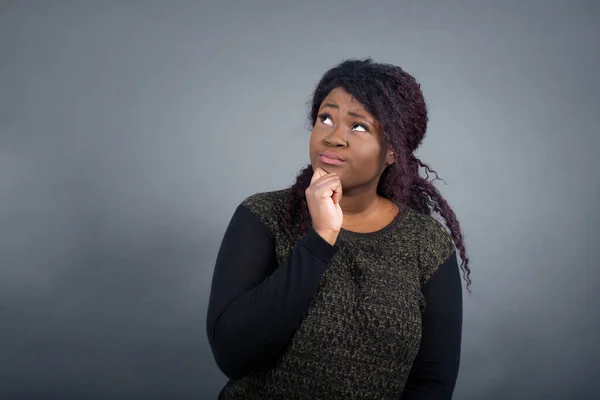 Portrait of thoughtful  woman keeps hand under chin, looks away trying to remember something or listens something with interest, dressed casually, poses indoors. Youth concept.