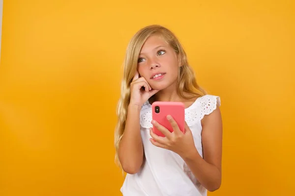 Słodkie Dziewczyna Gospodarstwa Smartfon Myślenie Żółtym Tle — Zdjęcie stockowe