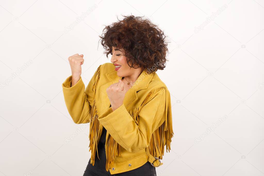 Caucasian brunette woman rejoicing her success and victory clenching her fists with joy. Lucky woman with hair bun being happy to achieve her aim and goals. Positive emotions, feelings.