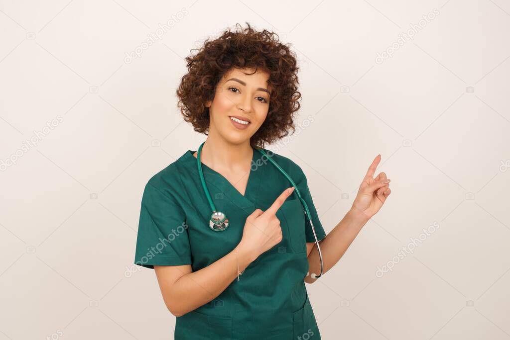 beautiful arab doctor woman  wearing medical uniform  with positive expression, wearing medical uniform, indicates with fore finger at blank copy space for your promotional text or advertisement.