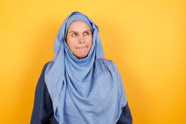 Şaşırmış orta yaşlı, tesettürlü Müslüman kadının fotoğrafı dudaklarını kıvırıyor ve endişeli görünüyor. Önünde korkunç bir şey görüyor, arka planda izole edilmiş.