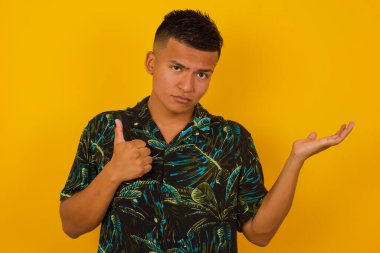 Genç, mutlu, İspanyol asıllı, neşeli bir adam başparmağını gösterip, diğer elini de evin içinde dururken işaret ediyor. İyi iş çıkardın. Günlük giysiler giyiyor..