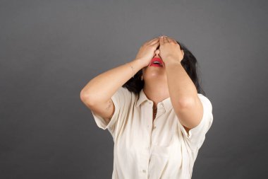 Güzel esmer kadın, elleri ve elleri ile gelişigüzel giyinmiş. Gri arkaplanda duruyor. 