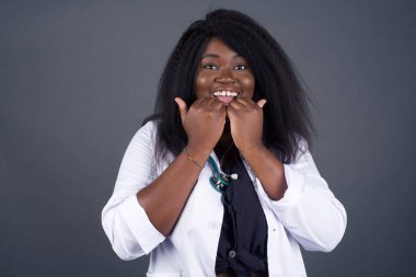 Mutlu Afrikalı Amerikalı kadın doktorların stüdyodaki görüntüleri çene altında el ele tutuşuyor, keyifli bir ruh hali içinde, ertesi günün arkadaş fikrini seviyor, gri duvarda izole edilmiş. Pozitif duygular.