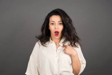 Güzel esmer kadın kayıtsızca giyinmiş, gri arka planda kendini gösteriyordu..  