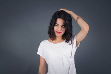 Güzel esmer kadın korkmuş ve pişmanlık dolu bir ifadeyle el ele tutuşuyor. Gri arka planda dikilen günlük giysiler giyiyor..