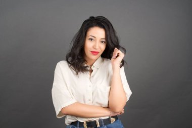 Gayri resmi giyinmiş güzel esmer kadın. Gri arkaplanda duruyor.  