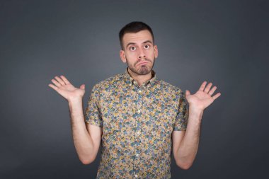 Modaya uygun olmayan bir adam şaşkınlık içinde omuz silker, karar vermeye çalışır, gri beton duvarın üzerinden neyi izole etmek istediğini şaşırtır. Tereddüt ve belirsizlik.