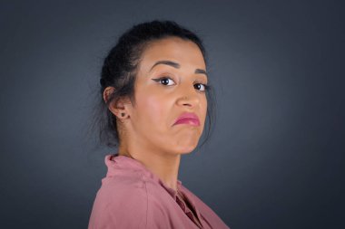 Züppe ifadeli güzel bir kadın dudaklarını kıvırıyor ve kaşlarını kaldırıyor şüpheli ve şüpheci bir ifadeyle şüpheli ve şüpheci bir ifadeyle bakıyor. Gri arka planda kapalı duruyor..