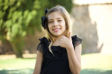 İyi iş! Mutlu gülümseyen mavi gözlü başarılı genç bir kızın portresi. Açık havada başparmak hareketi yapıyor. Olumlu insani duygu yüz ifadesi vücut dili. Komik kız.