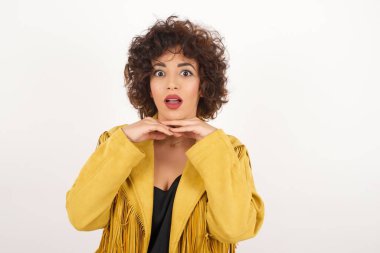 Stüdyoda aylak aylak dolaşıp zıplayan bir kadın. Sevimli kız elleriyle çeneye dokunuyor.