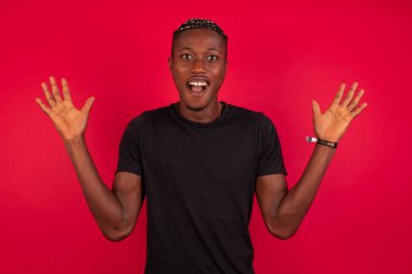 Başarı, başarı konsepti. Kırmızı arka plan üzerine siyah tişört giyen neşeli Afro-Amerikalı adam ellerini kaldırıyor, mutluluk dolu gözleri büyük başarılarını kutluyor. Çekici beyaz erkek resmi olarak giyinmiş..