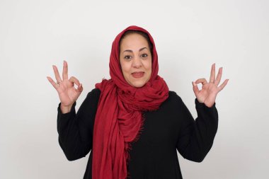 Olgun Müslüman kadının iki eliyle işaret göstermesi sevindirici bir ifade. Güzel bir kadının fotoğrafı çekici bir görünüme sahip, iyimser olmak. Gri duvara yaslanarak.