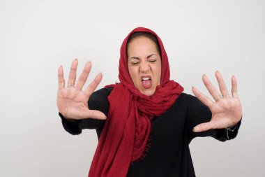 Tatmin olmayan kadın model kaşlarını çatar, iğrenç bir ifadeye sahiptir, dilini gösterir, itaatsizliğini gösterir, birilerine kızar, reddedenler bir şeyler yapar. Negatif yüz ifadesi. Stüdyoda poz veren başörtüsü takan orta yaşlı bir Arap kadın.