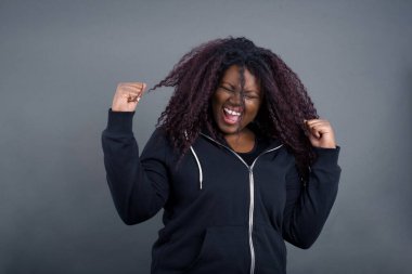 Güçlü, başarılı, kararlı, sıradan giysiler içinde, kollarını sıkan, yumruklarını sıkan, neşe ve heyecanla bağıran Afro-Amerikan kadınının portresi. Zafer, başarı ve başarı kavramı.