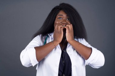 Endişe - güzel bir Afrikalı Amerikalı kadın doktorun kavramsal görüntüsü ağzını elleriyle kapayıp dışarıda dikilirken. Bir şeyden ya da birinden tırnak yemekten korktun mu?.