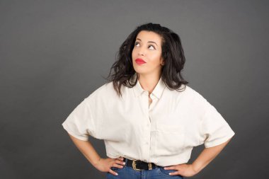 Gayri resmi giyinmiş güzel esmer kadın yukarı bakıyor. Gri arkaplanda duruyor. 