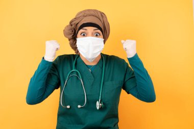 Yeşil tıp üniformalı genç, güzel, Müslüman doktor kadın başarısını ve zaferini sevinçle kutluyor. Şanslı kadın amacına ve hedeflerine ulaşmaktan mutlu..