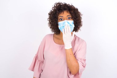 Yüz maskesi takan ve elini beyaz stüdyo arka planında gösteren bir kadın.