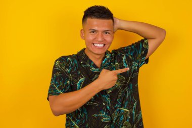 Neşeli genç adam bir şeyler gösteriyor. Bir eli kafasında, diğer eliyle işaret ediyor..