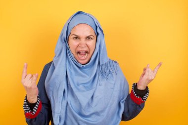 Bu dünyayı sallamak için doğmuşum. Neşeli orta yaşlı tesettürlü Müslüman kadın yüksek sesle bağırıyor ve kollarını kaldırarak ya da rock hareketleriyle gösteriyor. Konserde olmanın heyecanını dile getiriyor..