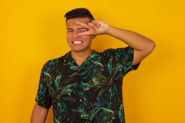 Yakışıklı, İspanyol asıllı, gözlerinin yanında V işareti yapan, sıradan kıyafetler giyen, duvarın karşısında duran adam..