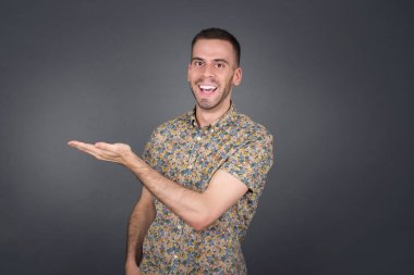 Pozitif memnun adam der ki: Vay be, ne kadar heyecan verici, hayret verici bir ifade, boş uzayda bir şey gösteriyor, açık elle izole edilmiş gri arkaplan üzerinde. Reklam kavramı.