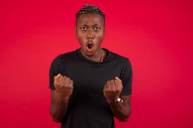 Güçlü, kararlı, siyah tişörtlü, kırmızı arka planda kazanan, kollarını kaldıran, yumruklarını sıkan, golü neşe ve heyecanla haykıran Afrikalı Amerikalı genç adamın belini kaldırın. Zafer, başarı ve başarı kavramı.