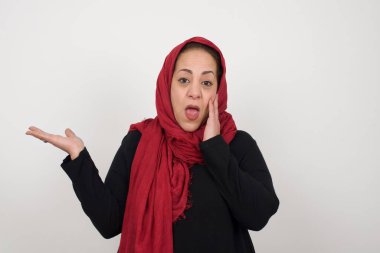 Pozitif sevinçli dişi der ki: Vay be, ne kadar heyecan verici, hayret verici bir ifade, bir şey ifade ediyor. Neşeli olgun bir kadın bir elini başının üstüne koyup diğer elini işaret eder. Stüdyoda poz veren başörtüsü takan orta yaşlı bir Arap kadın.