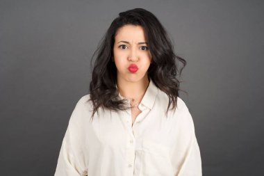 Güzel esmer kadın, gri arka planda gelişigüzel yanaklar üflüyor..  