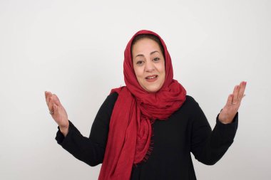 Neşeli kadın, beyaz arka planda izole edilmiş kollarını kaldırarak hoş bir jest yapıyor. Stüdyoda poz veren başörtüsü takan orta yaşlı bir Arap kadın.
