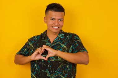 Güzel İspanyol bir adam izole edilmiş arka planda. Sevgiyle gülümsüyor. Elleriyle kalp sembolü ve şekli gösteriyor. Romantik konsept.