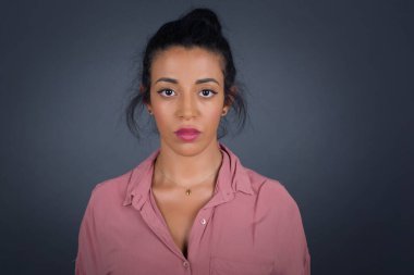 Neşeli esmer kadın kameraya bakıyor, bir şey düşünüyor. Gri stüdyoda duruyor.. 