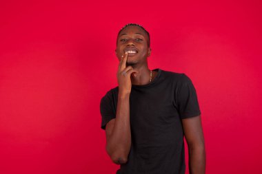 Hayalperest Afro-Amerikan adam, düşünceli bir ifadeyle, kameraya bakıyor, elini yüzüne yaklaştırıyor, parmağını ısırıyor, hoş bir şey düşünüyor, duvara karşı poz veriyor..