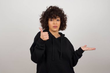 Genç, mutlu, neşeli bir kadın baş parmağını gösterip diğer elini boş uzayı işaret ediyor.