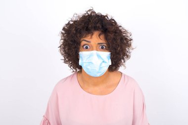 Yüz maskesi takan ve günlük kıyafet giyen bir kadın beyaz stüdyo arka planında izole edilmiş.