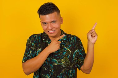 Reklam konsepti. Arka planda ışıldayan tebessümü olan pozitif, güzel İspanyol adam işaret parmağıyla işaret ediyor ve boş fotokopi odasına bakıyor..