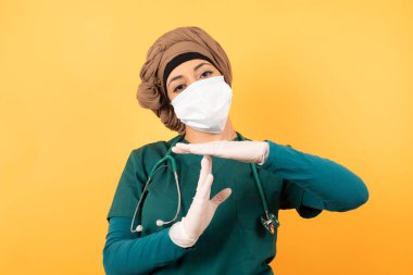 Yeşil üniformalı, genç, güzel, Müslüman doktor kadın yorgun ve sıkkın bir jest yapıyor. İş stresi ve zaman kavramı yüzünden durmak zorunda. Gri duvara yaslanarak.