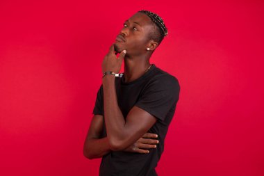 Düşünceli gülümseyen Afrikalı Amerikalı adamın portresi elini çenesinin altında tutuyor, yan bakıyor, ilginç bir şey düşünüyor ya da merak ediyor, sıradan giyiniyor, stüdyoya karşı poz veriyor. Karar alma kavramı.