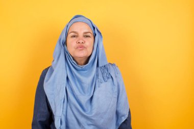 Hoş görünümlü, tesettürlü, orta yaşlı Müslüman bir kadın. Dudaklarını öpecek gibi tutuyor. Yüzü asık, mutlu bir ifade takınıyor.. 