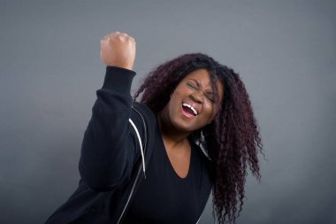 Vahşi, kendine güvenen Afro-Amerikan kadını. Önünde yumruğunu tutarak dövüşmeye ya da meydan okumaya hazır gibi. Bağırıyor ve yüzünde agresif bir ifade var. Gri arkaplan üzerinde izole.