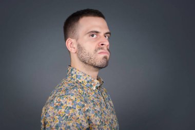 Züppe ifadeli güzel bir adam dudaklarını kıvırıyor ve kaşlarını kaldırıyor şüpheli ve şüpheci bir ifadeyle şüpheli ve şüpheci bir ifadeyle bakıyor. Gri arka planda kapalı duruyor..