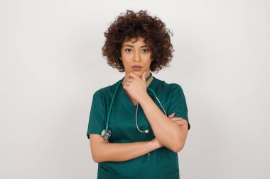 Çenesinin altında eli olan düşünceli gülümseyen bir doktorun portresi doğrudan kameraya bakıyor.