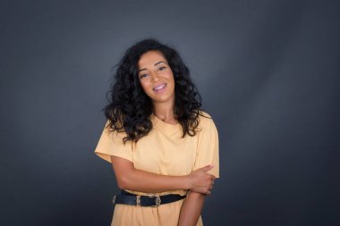 Sevimli, iyi huylu, esmer bir kadın. Sevgi ve sempati göstermek için kendini tutarak büyüleyici bir gülümseme ve dostça bir ifade takınıyor..